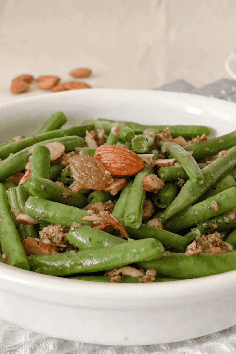 Air fryer green beans almondine with toasted sliced almonds and lemon zest on a white serving plate