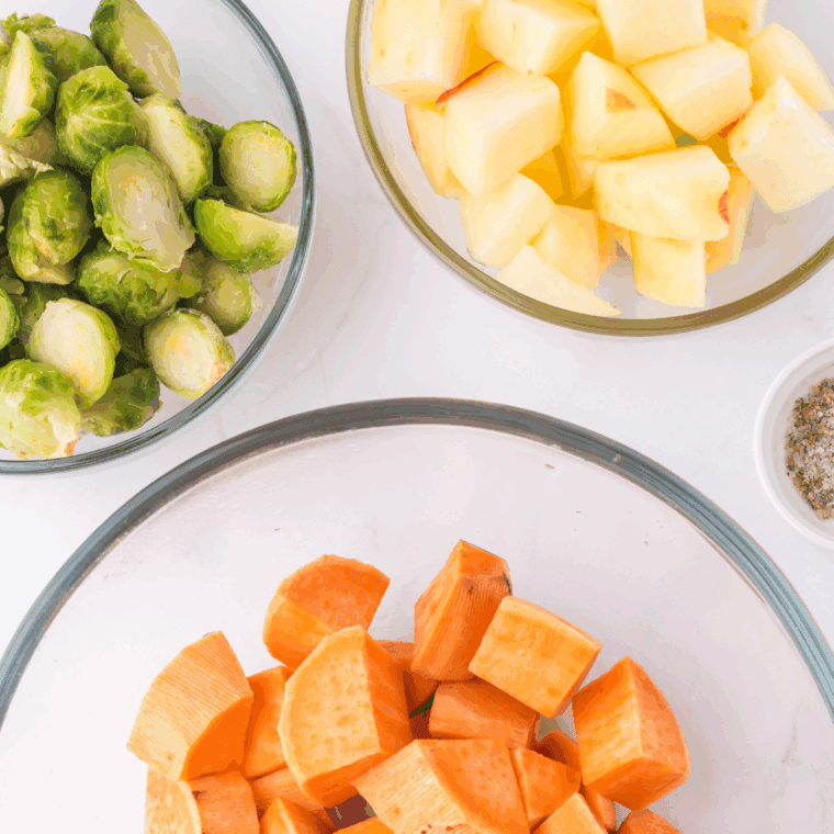 Chopped sweet potatoes, Brussels sprouts, and apples in mixing bowls.