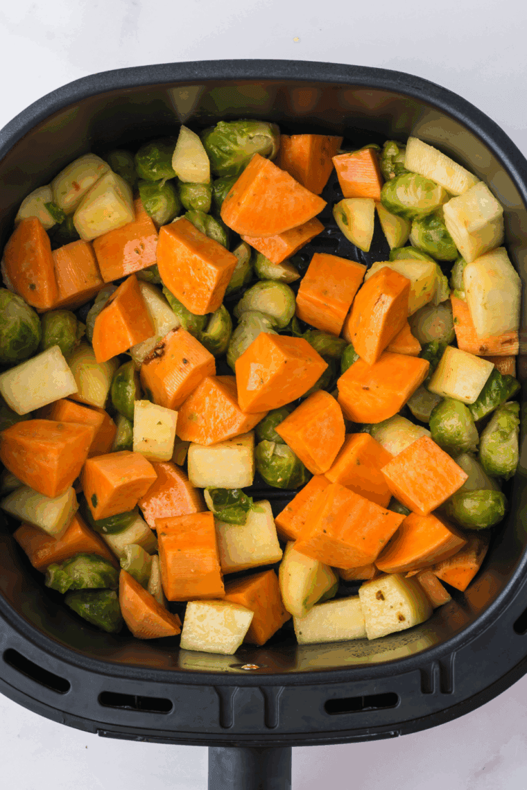 Veggies and apples tossed with oil and garlic salt inside the air fryer basket.