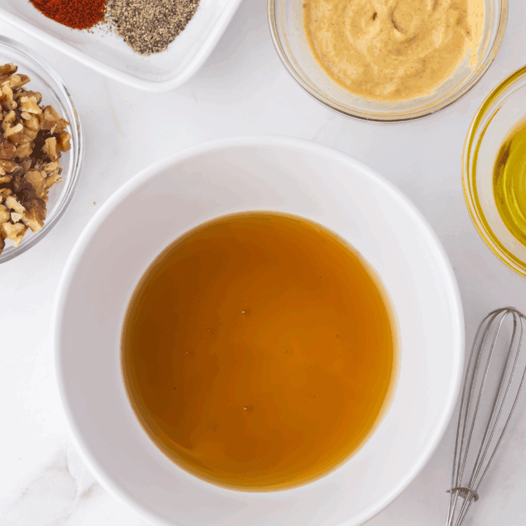 Mixing walnut topping ingredients—walnuts, Dijon, maple syrup, olive oil, and spices—in a bowl.