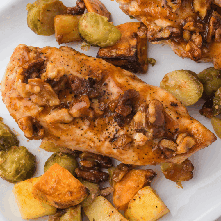 Golden air fryer chicken coated in crushed walnuts and drizzled with maple syrup, served on a white plate.