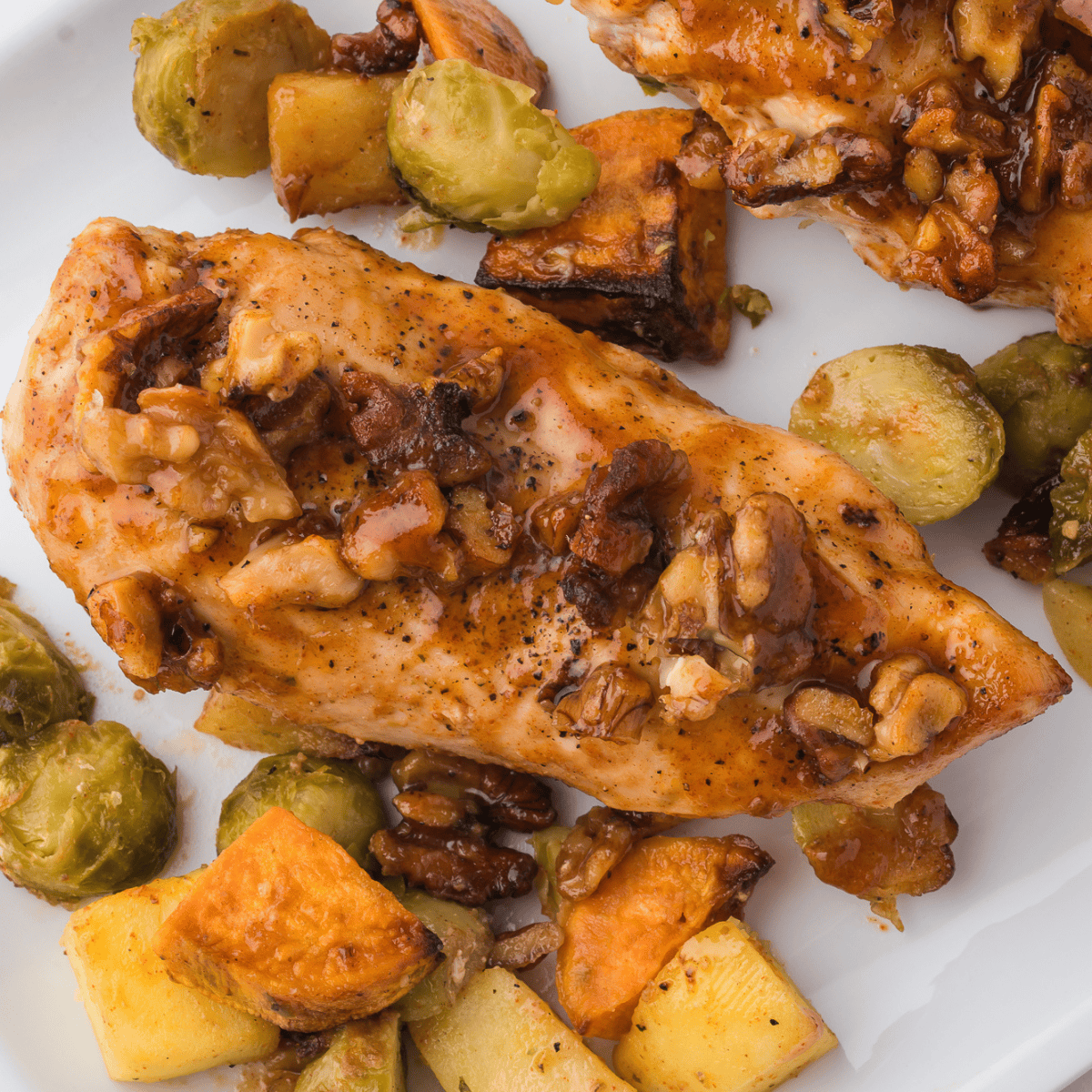 Golden air fryer chicken coated in crushed walnuts and drizzled with maple syrup, served on a white plate.