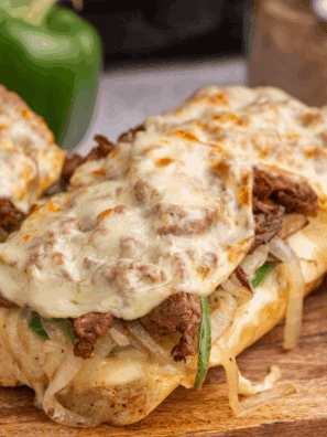 Air fryer Philly cheesesteak cheesy bread topped with sliced steak, melted cheese, peppers, and onions on a toasted baguette.
