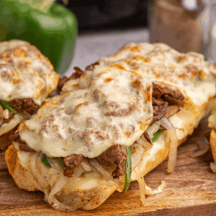 Air fryer Philly cheesesteak cheesy bread topped with sliced steak, melted cheese, peppers, and onions on a toasted baguette.