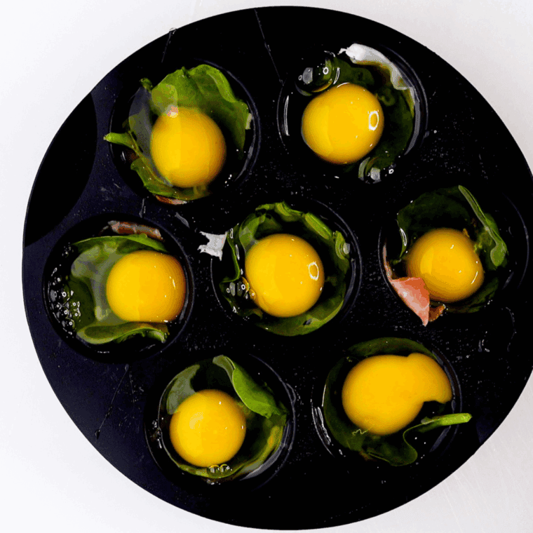 Cracked eggs in muffin cups with salt, pepper, and crumbled goat cheese sprinkled on top.