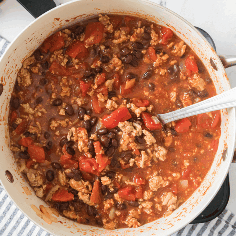 Adding beans, diced tomatoes, tomato paste, spices, and water to the pot, simmering until the sweet potatoes are fully baked, and adjusting seasoning to taste.