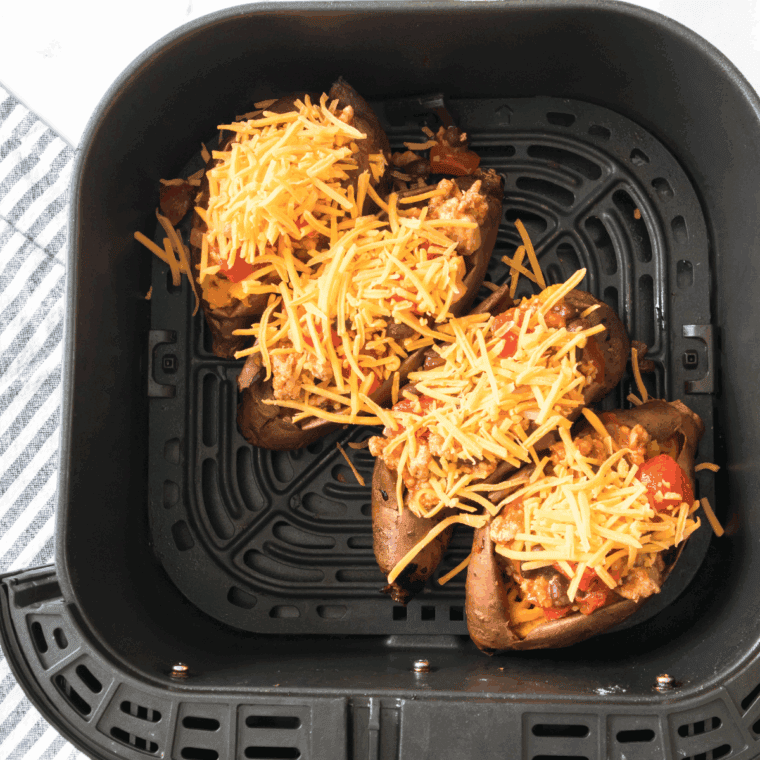 Cutting sweet potatoes lengthwise, mashing the insides, topping with chili and cheese, then baking until melted, and garnishing with cilantro and sliced green onions.