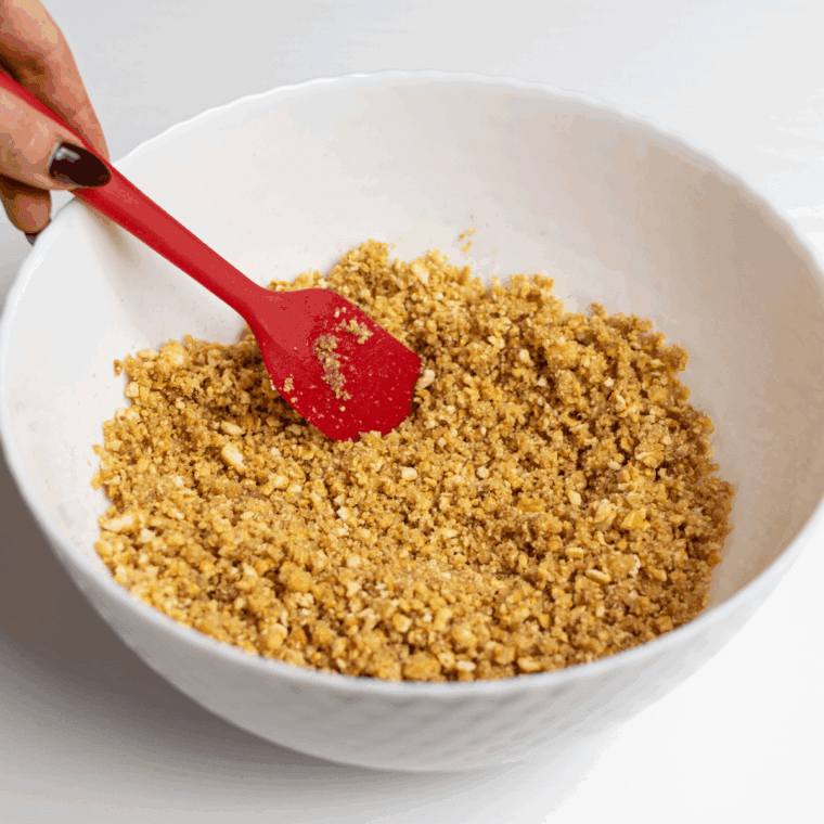 Combining graham crackers, sugar, cinnamon, and melted butter to form a crust in a round cake pan.