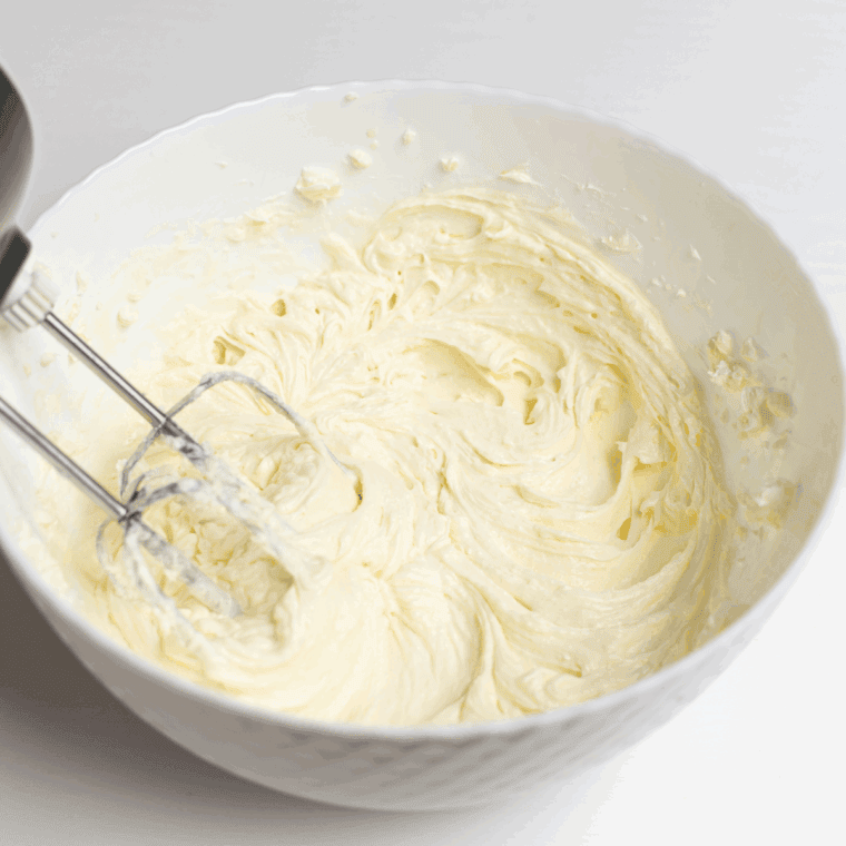 Mixing softened cream cheese, sugar, vanilla, eggs, sour cream, heavy cream, and flour until smooth and fully blended with an electric mixer.