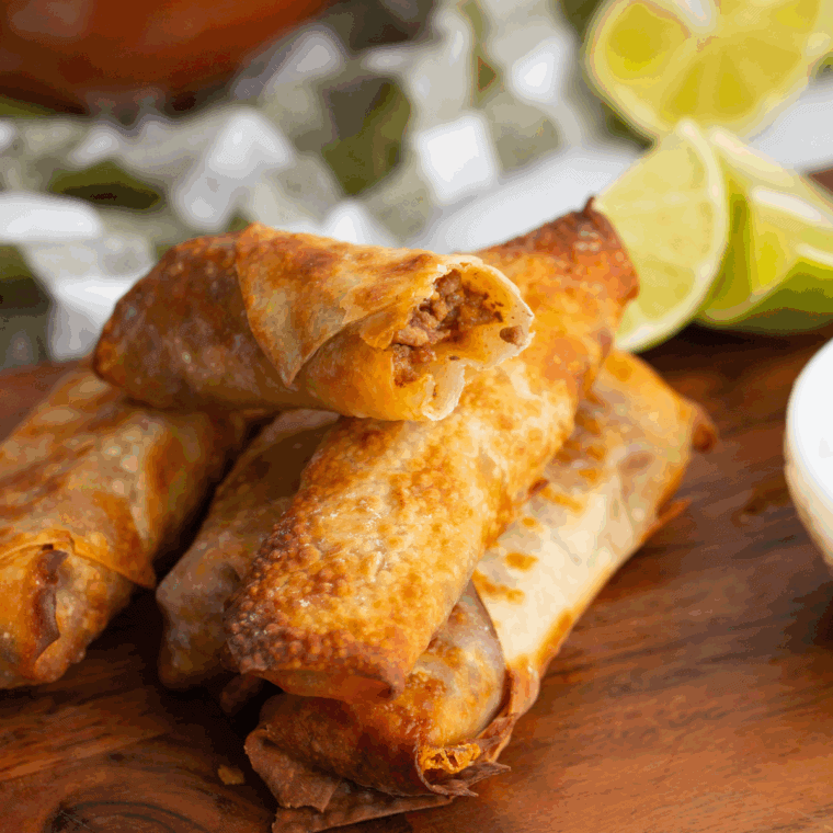 Close-up of crispy homemade egg rolls filled with seasoned pork and shredded cabbage on a plate with dipping sauce.