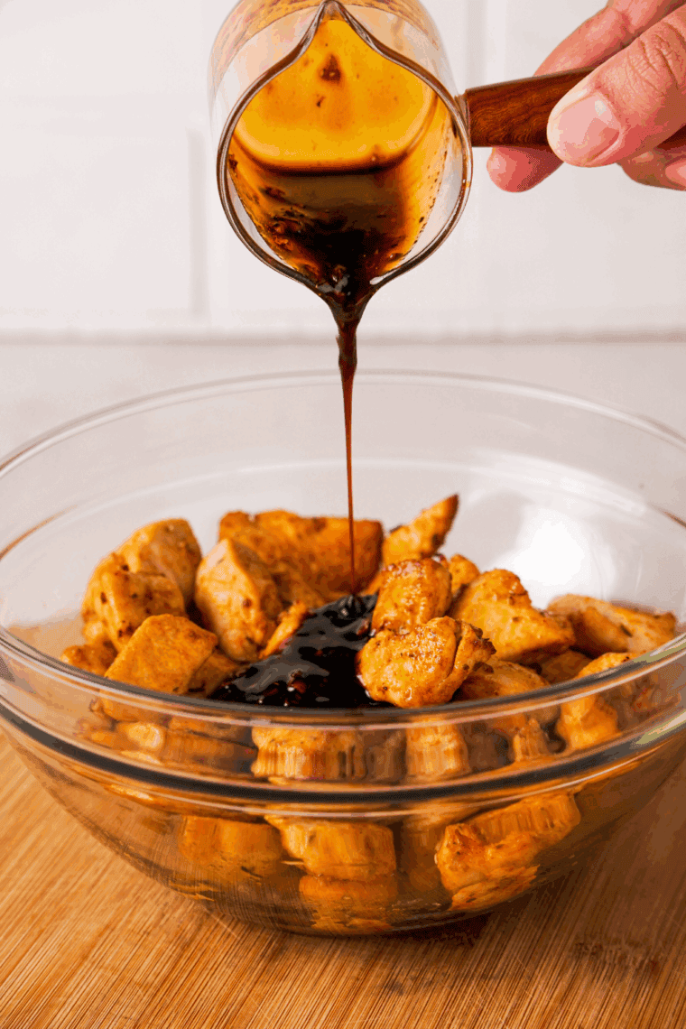 Bowl with soy sauce, brown sugar, garlic, and spices being whisked for marinade with raw chicken thighs beside it.