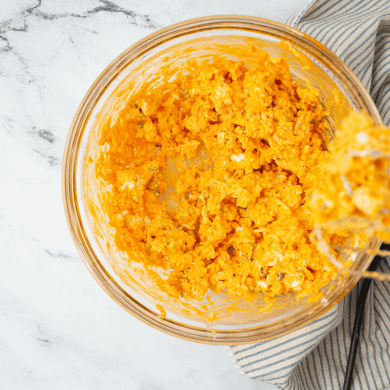 Folding shredded cheddar and mozzarella cheese into the buffalo chicken mixture.