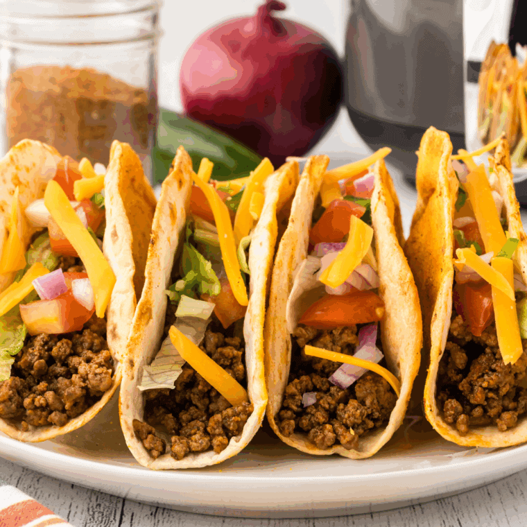 Golden crispy tacos filled with seasoned beef, melted cheese, lettuce, and taco sauce on a white plate.