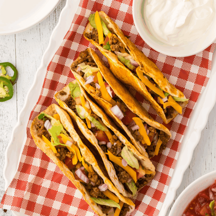 Golden crispy tacos filled with seasoned ground beef, melted American cheese, lettuce, and taco sauce on a plate.