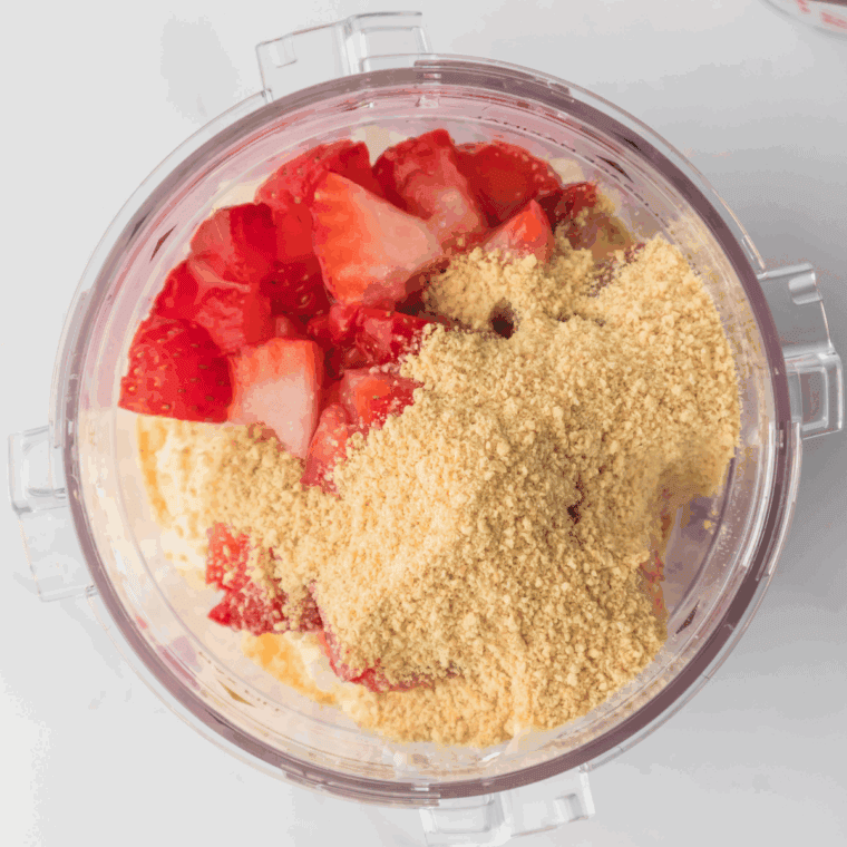 Ingredients in the Ninja Creami pint container, including vanilla ice cream, cheesecake filling, strawberries, crushed graham crackers, and milk, ready to blend.