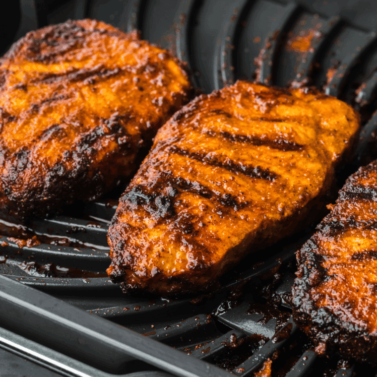 Juicy pork chops grilled in the Ninja Foodi Grill, garnished with herbs and served on a plate with vegetables.