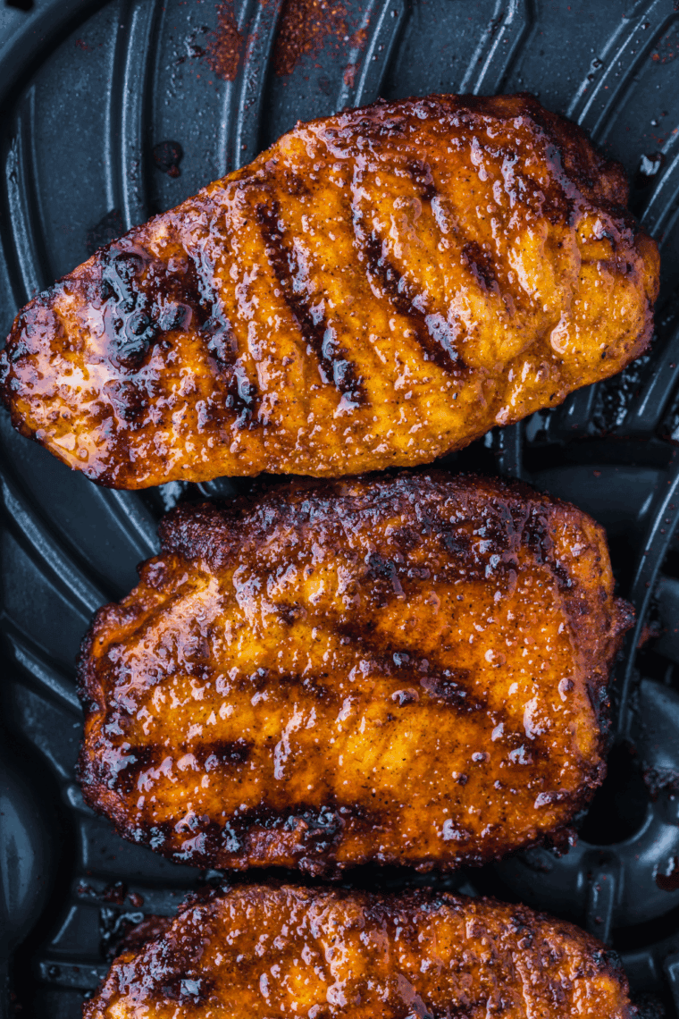 Grilled pork chops cooked in the Ninja Foodi Grill, served on a plate with fresh herbs and vegetables.