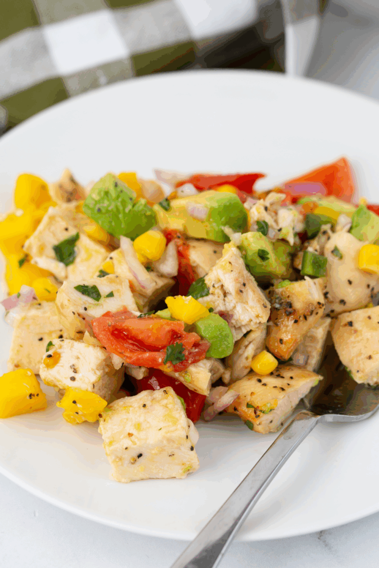 Colorful avocado chicken mango salad served in a white bowl with grilled chicken, diced mango, avocado, corn, tomatoes, and red onion.
