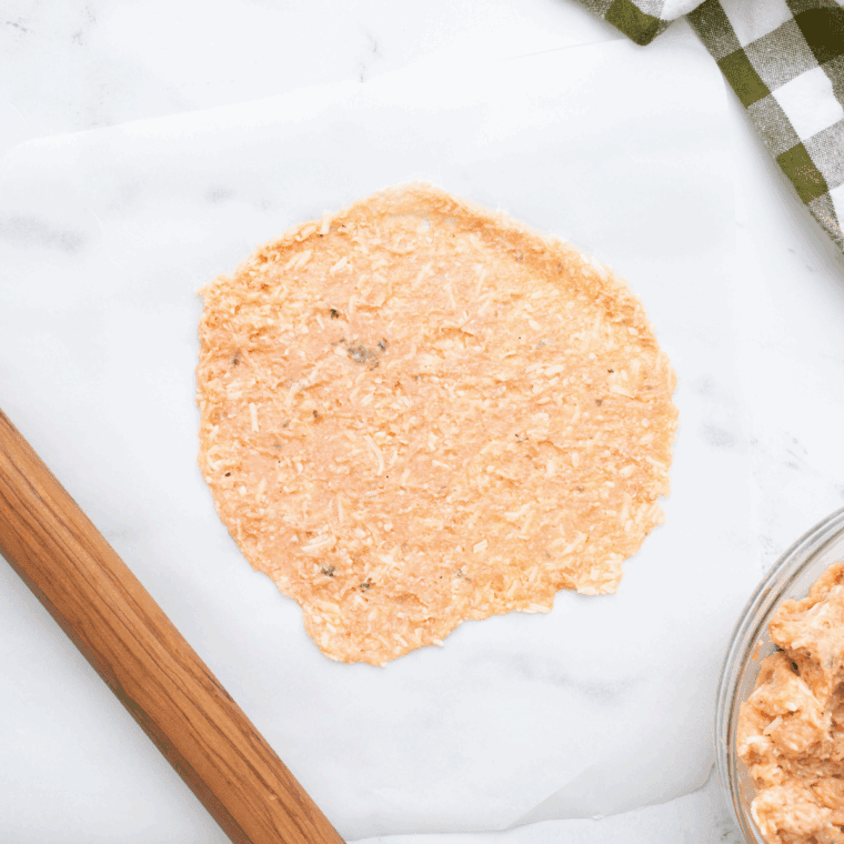 Rolling chicken crust mixture into a 6-inch round on parchment paper.