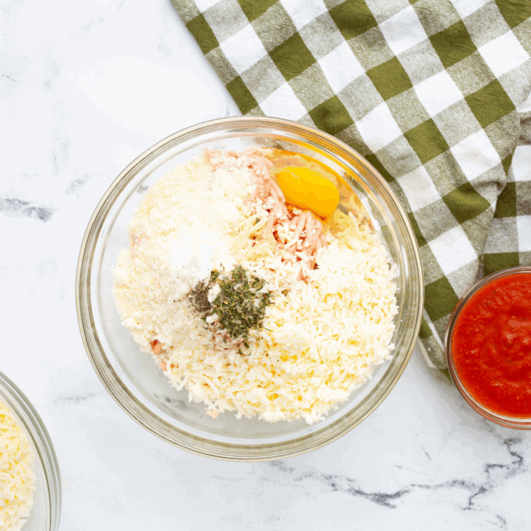 Mixing ground chicken, cheeses, and seasonings in a bowl for pizza crust.