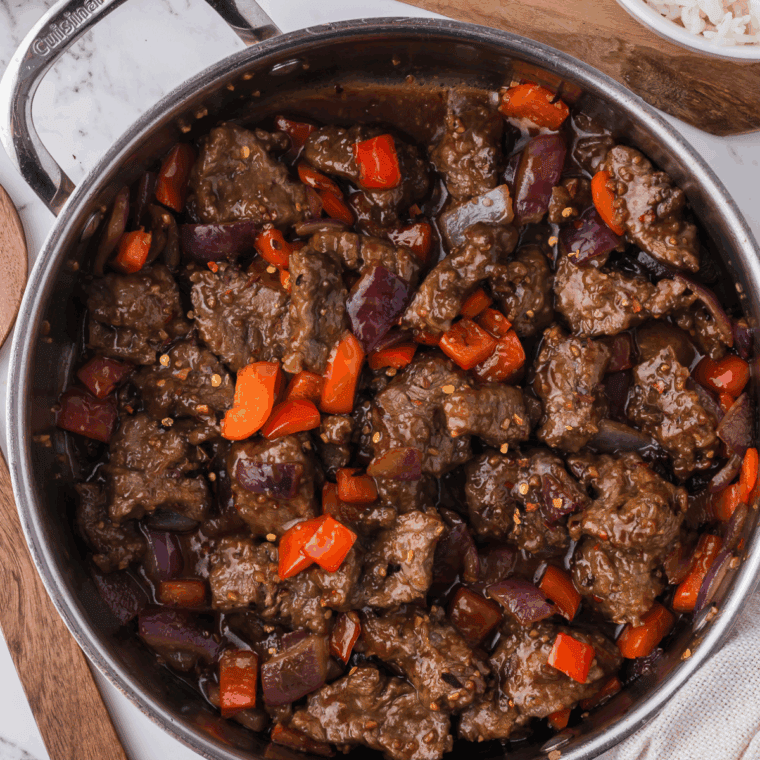 Crispy air fryer Beijing beef with peppers in glossy sauce on a plate.