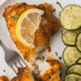 Crispy, golden-brown air fryer monkfish fillets served with lemon wedges and herbs.