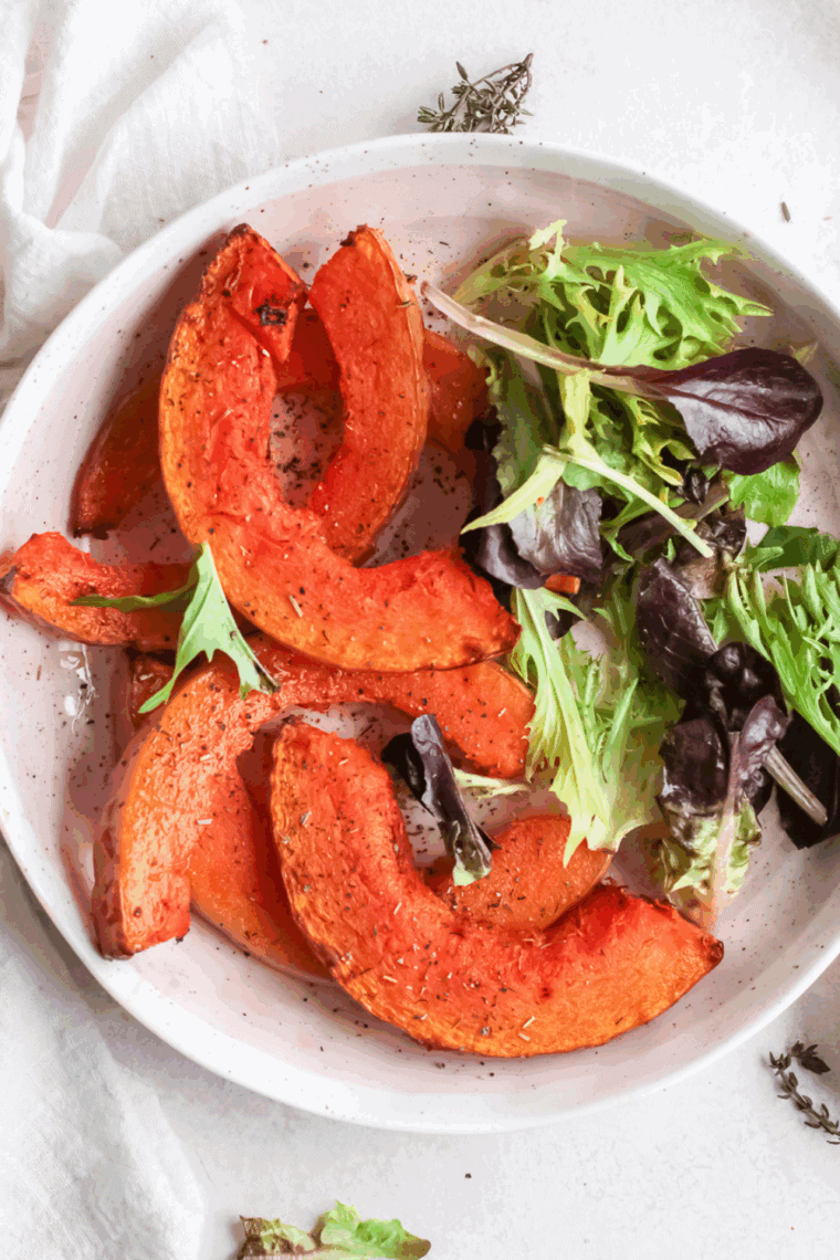 Crispy air fryer pumpkin wedges garnished with herbs on a serving plate.