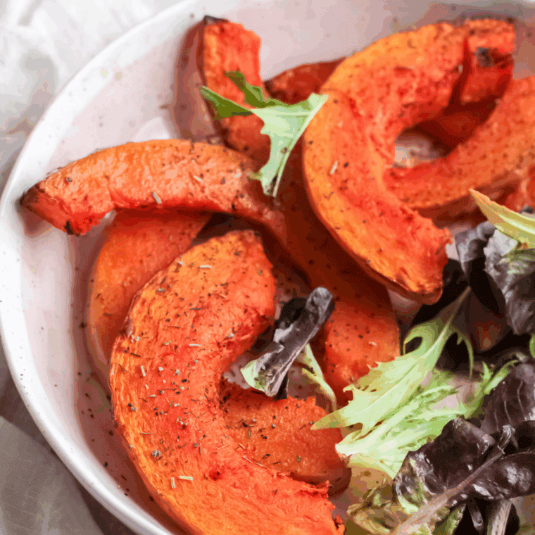 Golden-brown air fryer pumpkin wedges on a plate with dipping sauce.