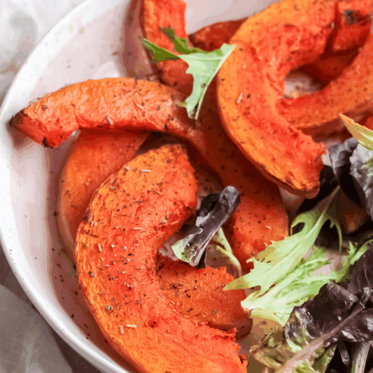 Golden brown air fryer pumpkin wedges served on a plate with herbs and dipping sauce.