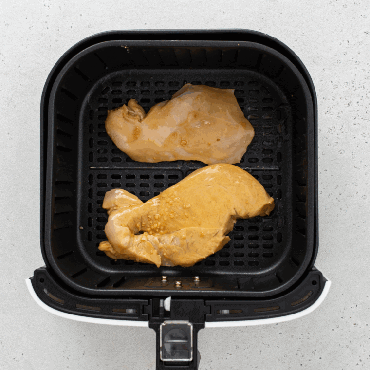 Placing marinated chicken breasts in air fryer basket preheated to 370°F.