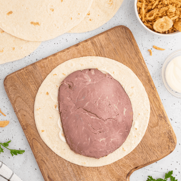 Assembling wrap with horseradish, cheese, onions, and roast beef.