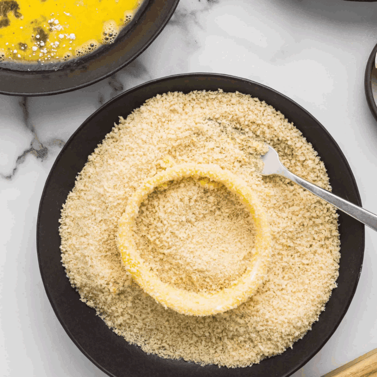 Onion rings being coated and pressed into panko breadcrumbs.