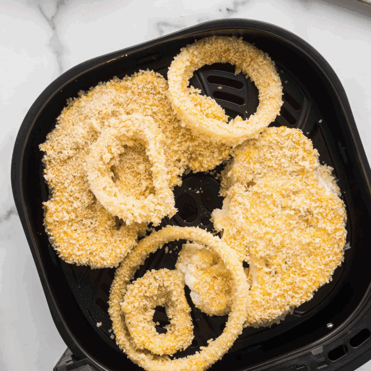Onion rings cooking in air fryer basket until golden and crispy.