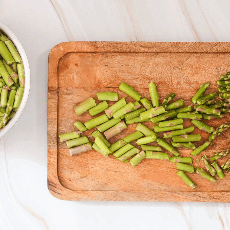 Fresh asparagus spears on a cutting board, ends trimmed and cut into bite-sized pieces.