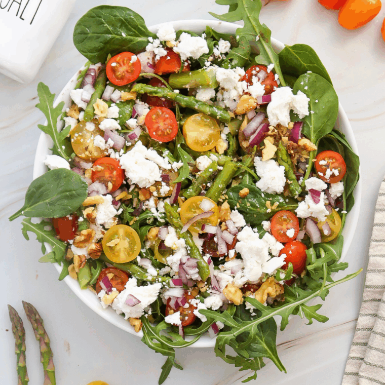 Bowl of asparagus salad with goat cheese, spinach, cherry tomatoes, and lemon dressing.