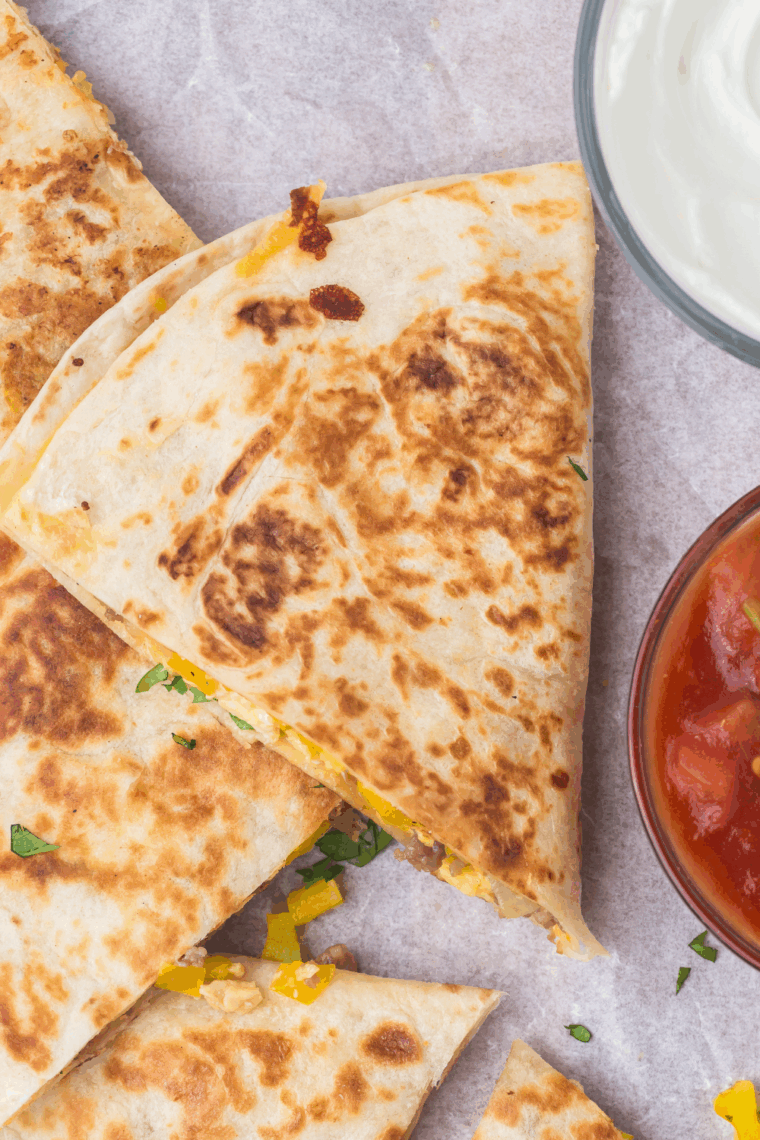 Golden brown breakfast quesadillas cooking on a Blackstone griddle, filled with eggs, sausage, and melted cheese.