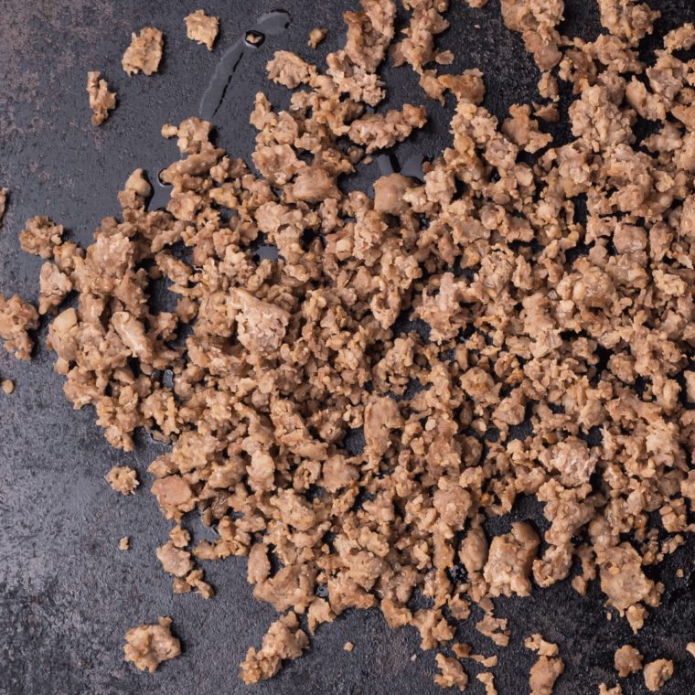 Crumbled breakfast sausage cooking on a Blackstone griddle until browned.