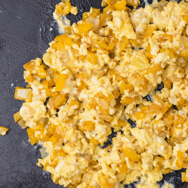 Scrambled eggs cooking next to vegetables on the griddle.