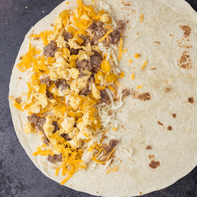 Tortilla filled with cheese, sausage, eggs, and veggies on griddle.