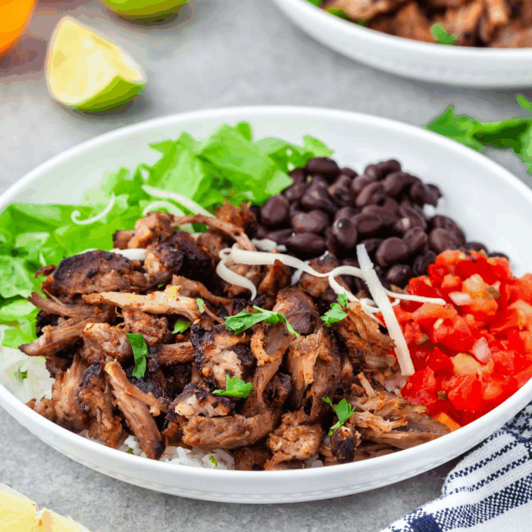 Carnitas Burrito Bowl with shredded carnitas meat, black beans, diced tomatoes and lettuce. All served in a white bowl.