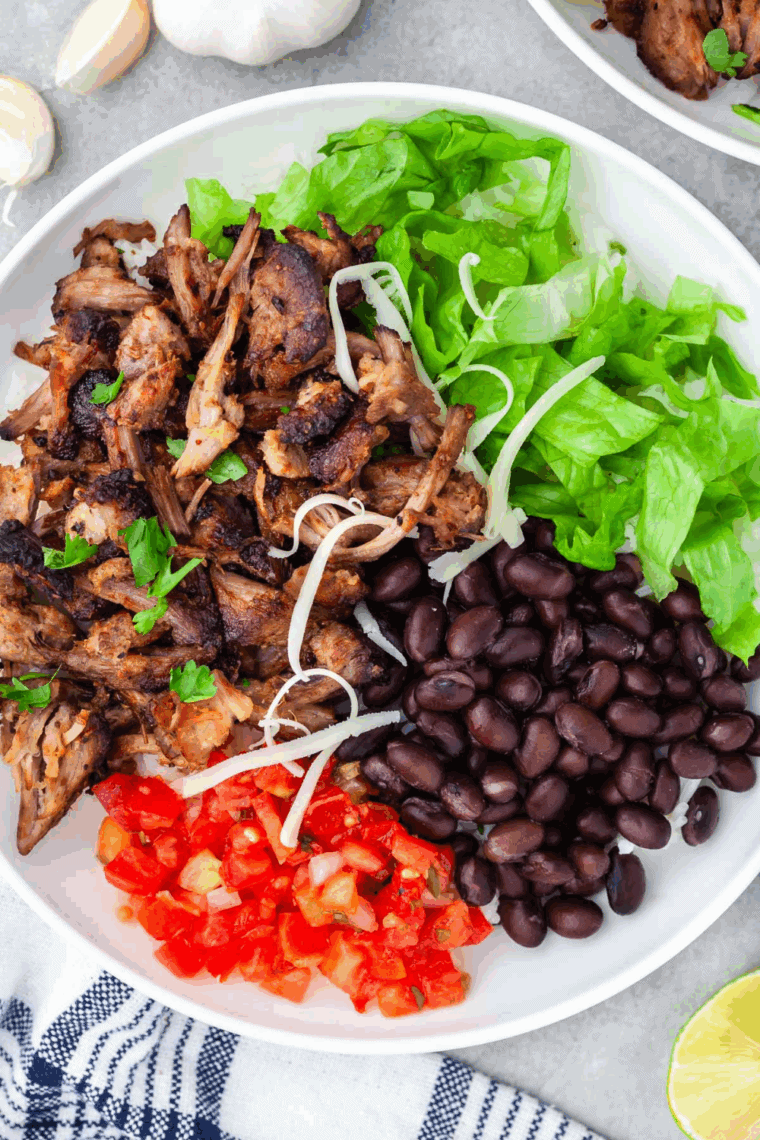 Carnitas Burrito Bowl on the counter filled with toppings in white bowl.