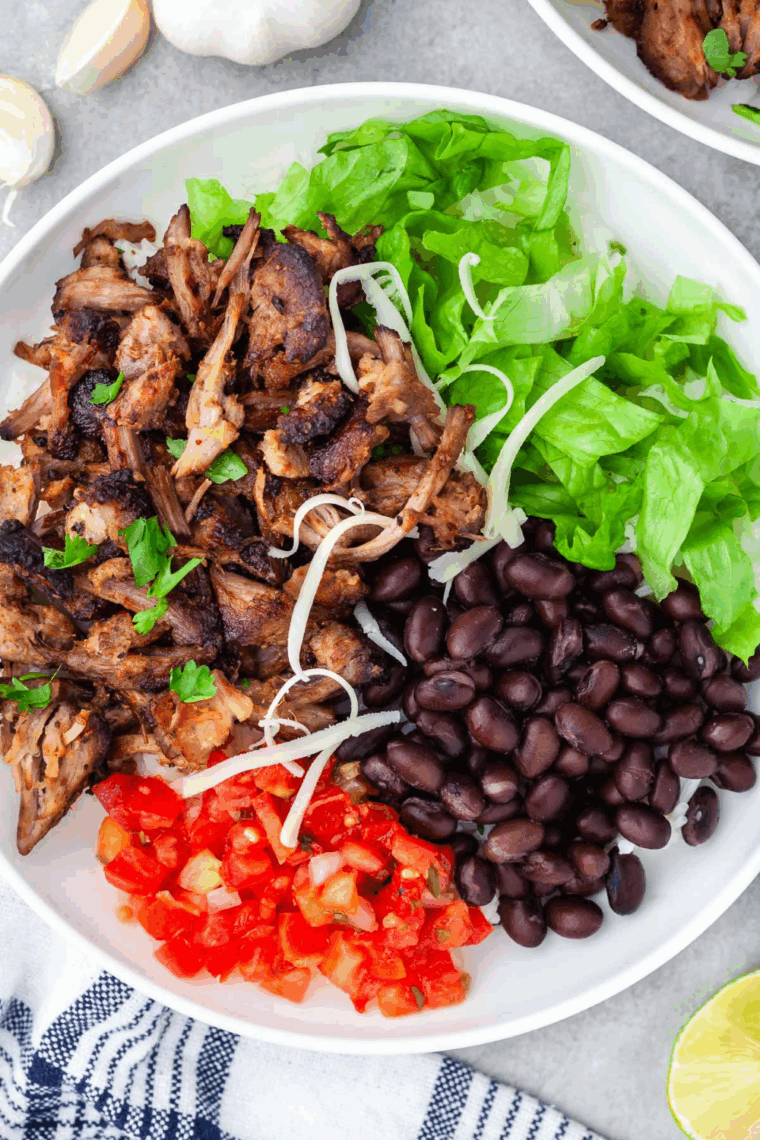 Plate of Carnitas Burrito Bowl with lettuce, cheese, black beans, and carnitas meat in a large white bowl.
