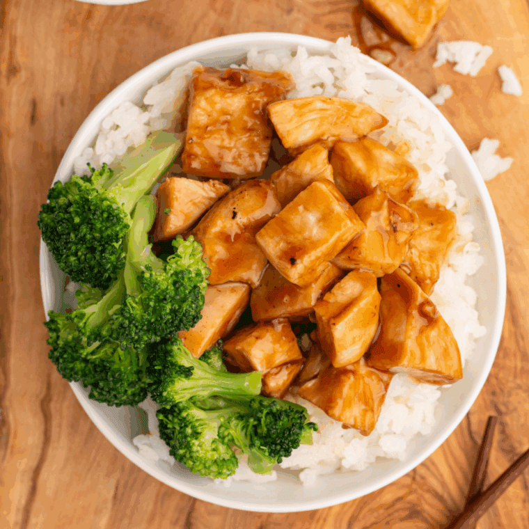 Sliced chipotle honey chicken served on a wooden board with lime wedges and fresh herbs.