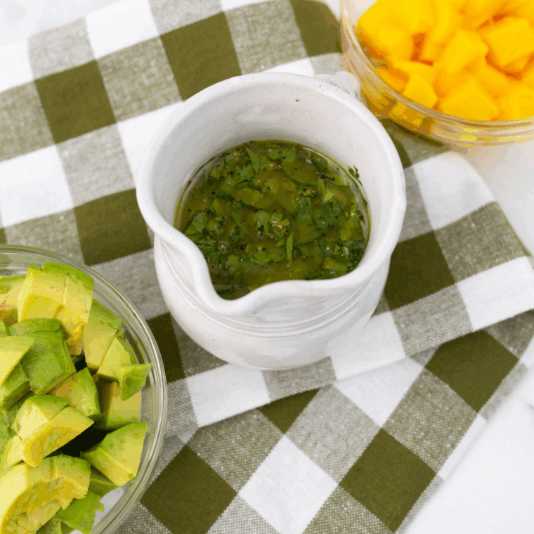 Bowl of homemade cilantro lime jalapeño vinaigrette surrounded by fresh lime, cilantro, and sliced jalapeños.

