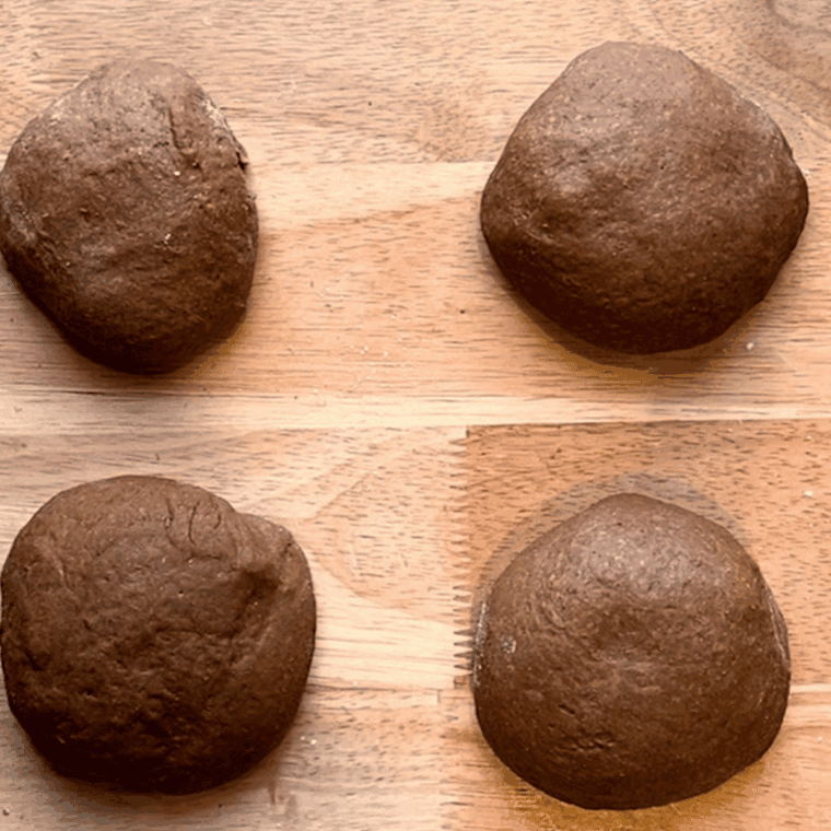 Shaped brown bread dough rising on a parchment-lined baking sheet before baking.