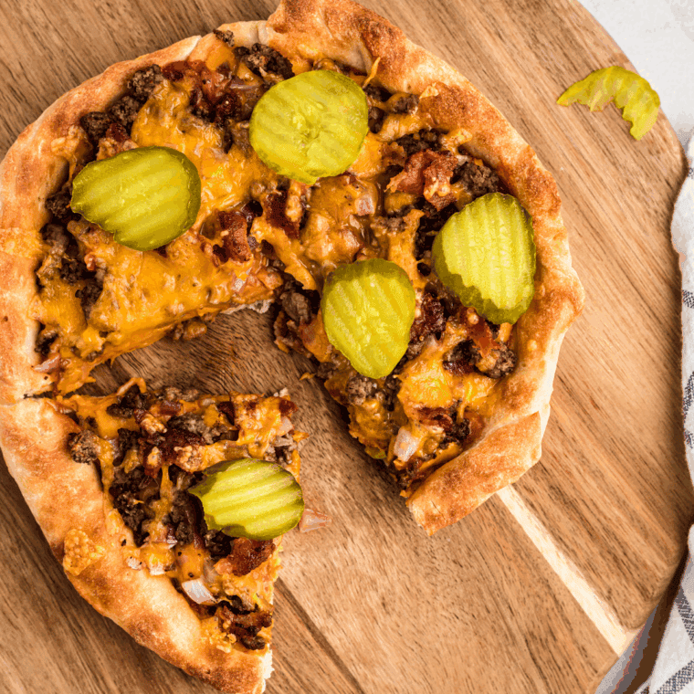 Homemade cheeseburger pizza topped with ground beef, cheddar, onions, pickles, and sauce on a golden crust.