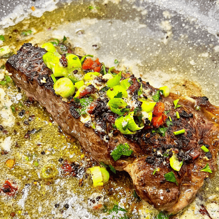 Cooked Cowboy Butter Steak with fresh herbs and veggies.
