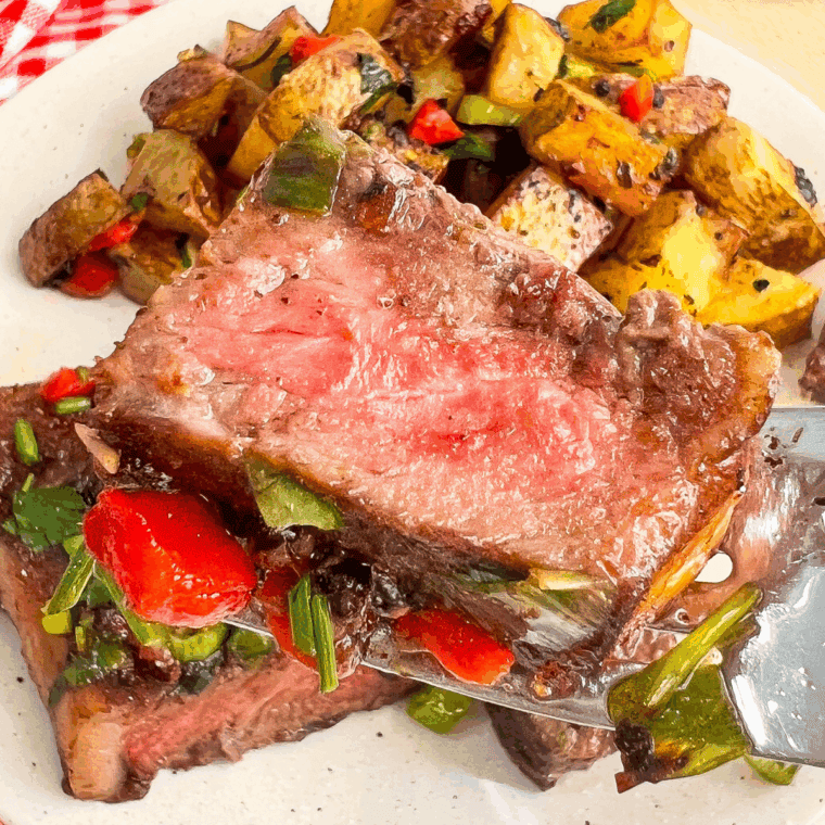 Plate of Cowboy Butter Steak and crispy potatoes drizzled with garlic herb butter.