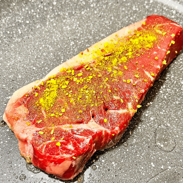 Searing steak in a hot skillet with olive oil, then adding butter, garlic, green onions, and pimentos.