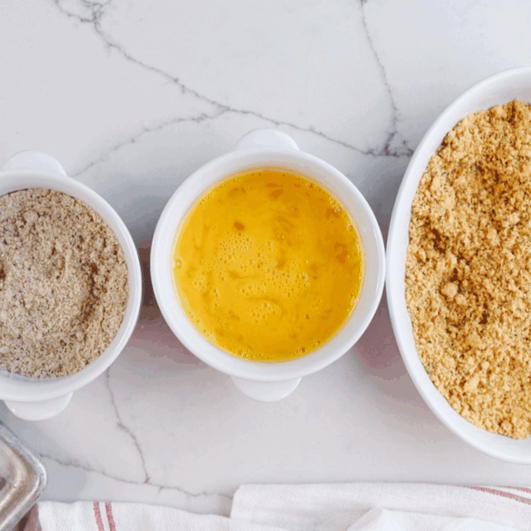 Three bowls for breading mozzarella sticks: flour, egg wash, and seasoned breadcrumbs.